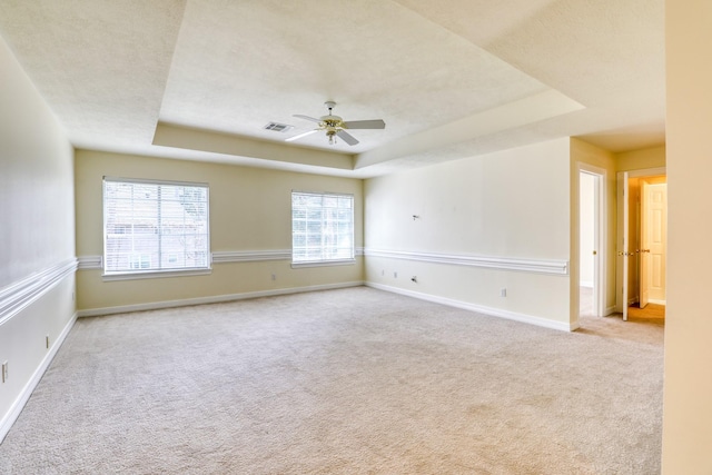 carpeted spare room featuring visible vents, baseboards, a textured ceiling, a raised ceiling, and a ceiling fan