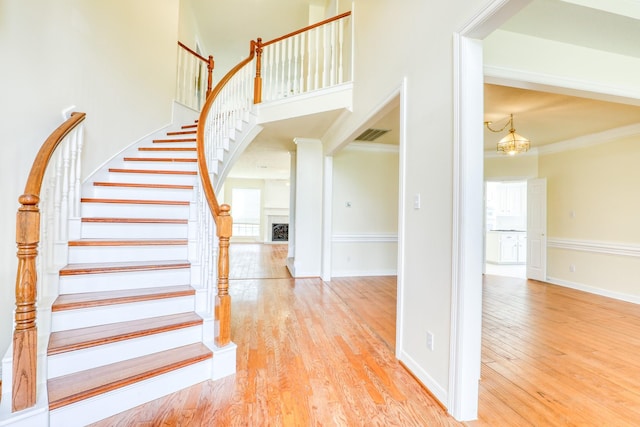 staircase featuring crown molding, baseboards, a fireplace, a towering ceiling, and wood finished floors