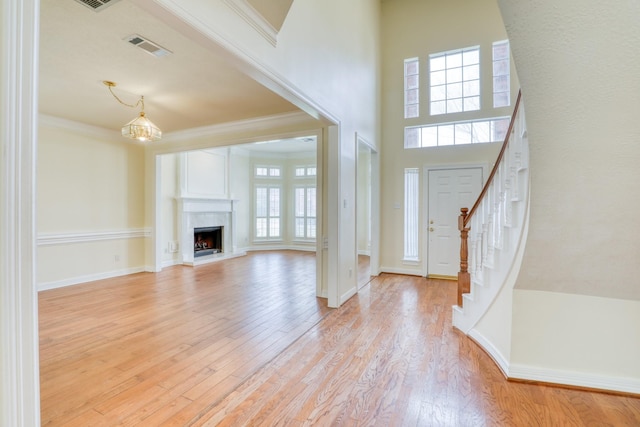 entrance foyer with visible vents, stairway, crown molding, light wood finished floors, and a premium fireplace