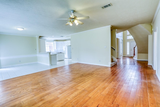 unfurnished living room featuring light wood-type flooring, visible vents, stairs, and crown molding