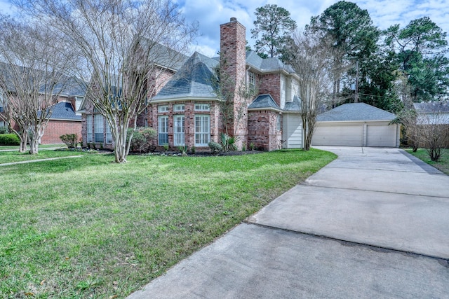 view of front of house featuring a front lawn, a detached garage, an outdoor structure, brick siding, and a chimney