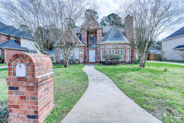 view of front of house with brick siding, a chimney, a front lawn, and a shingled roof