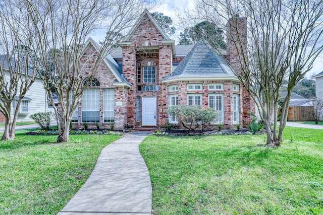 view of front of home with a front yard, a chimney, brick siding, and a shingled roof