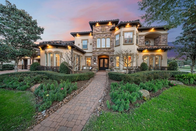 mediterranean / spanish house featuring a balcony, stone siding, a tile roof, french doors, and stucco siding