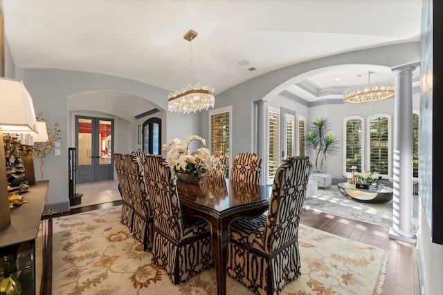 dining area with arched walkways, light wood-style flooring, decorative columns, and a notable chandelier