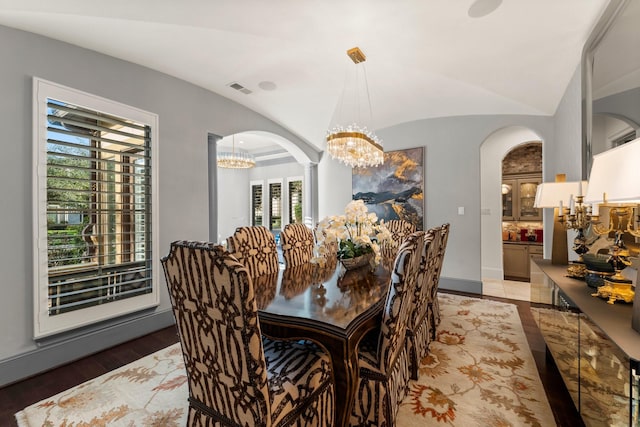 dining room featuring visible vents, arched walkways, lofted ceiling, wood finished floors, and a notable chandelier