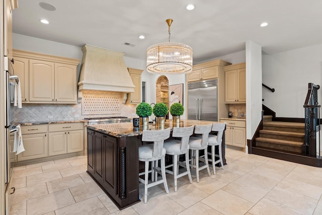 kitchen with a kitchen island, dark stone countertops, custom exhaust hood, stainless steel appliances, and cream cabinetry