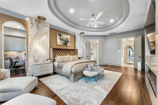 bedroom featuring connected bathroom, dark wood finished floors, baseboards, a raised ceiling, and crown molding