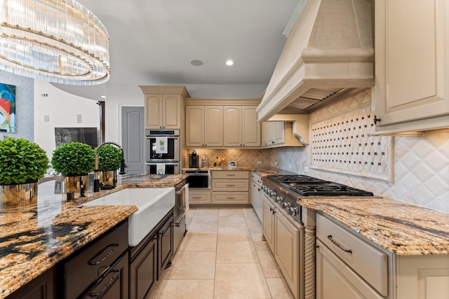 kitchen featuring cream cabinetry, appliances with stainless steel finishes, custom exhaust hood, decorative backsplash, and light stone countertops