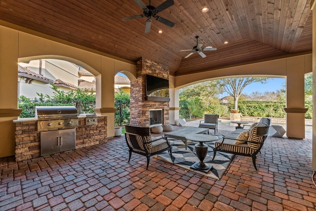 view of patio / terrace featuring a ceiling fan, a grill, fence, exterior kitchen, and an outdoor living space with a fireplace