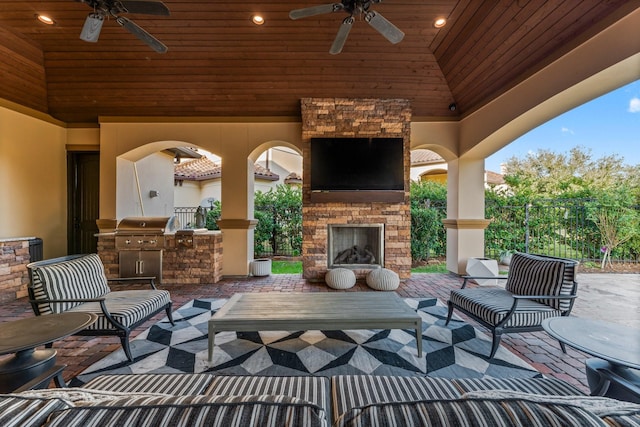 view of patio with fence, a ceiling fan, exterior kitchen, grilling area, and an outdoor living space with a fireplace