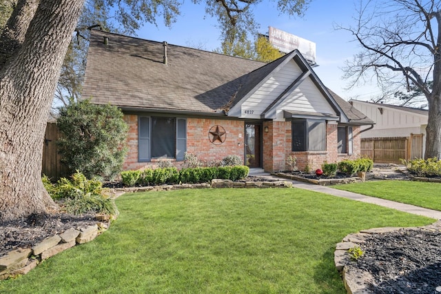 view of front of property featuring brick siding, roof with shingles, a front yard, and fence