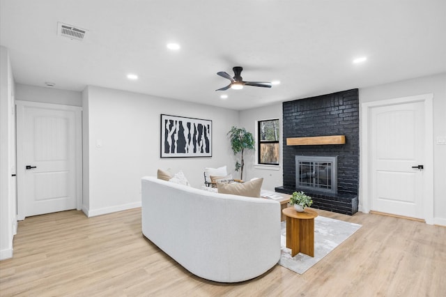 living room with visible vents, light wood-style floors, a brick fireplace, and ceiling fan