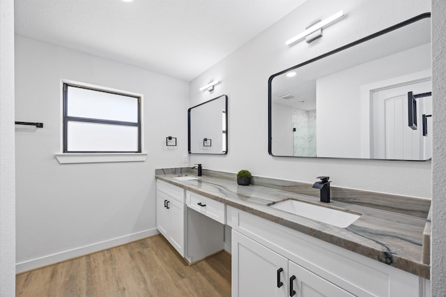 full bathroom with walk in shower, baseboards, double vanity, wood finished floors, and a sink