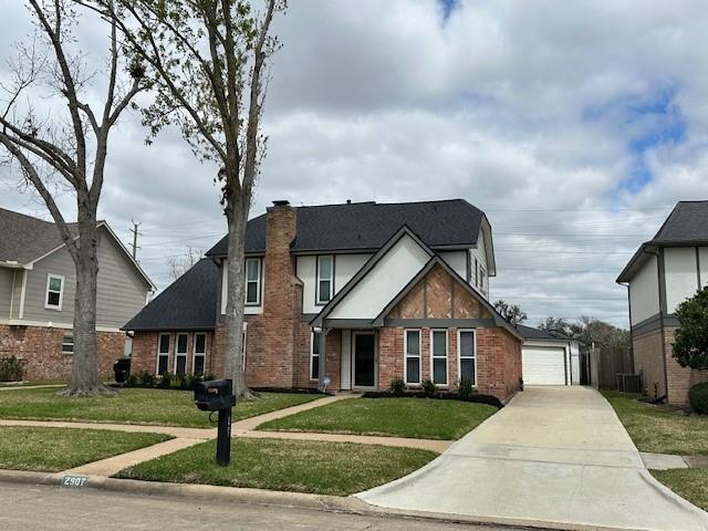 tudor home with brick siding, a chimney, a detached garage, and a front yard