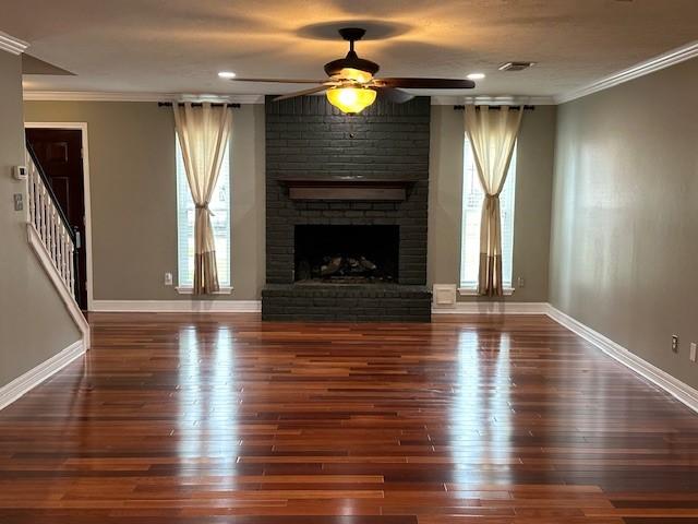 unfurnished living room with plenty of natural light, ornamental molding, a fireplace, and wood finished floors