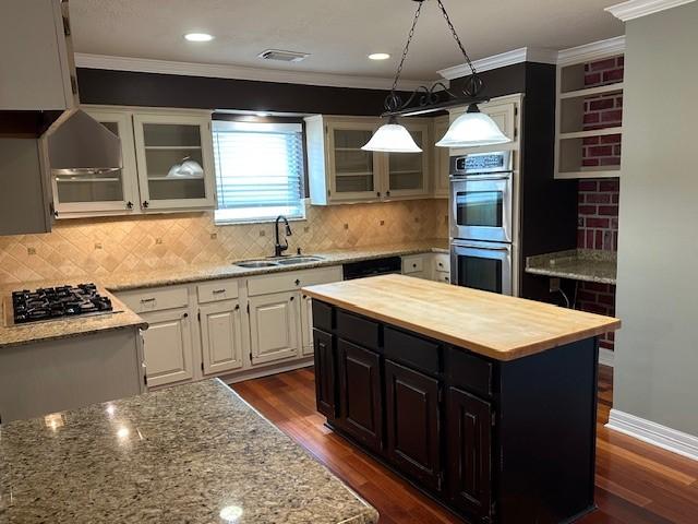 kitchen featuring butcher block counters, a kitchen island, appliances with stainless steel finishes, crown molding, and a sink