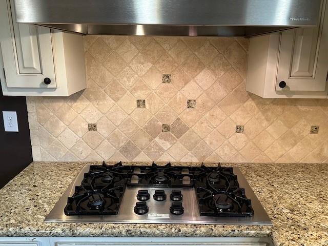 kitchen with tasteful backsplash, stainless steel gas cooktop, wall chimney range hood, and light stone countertops