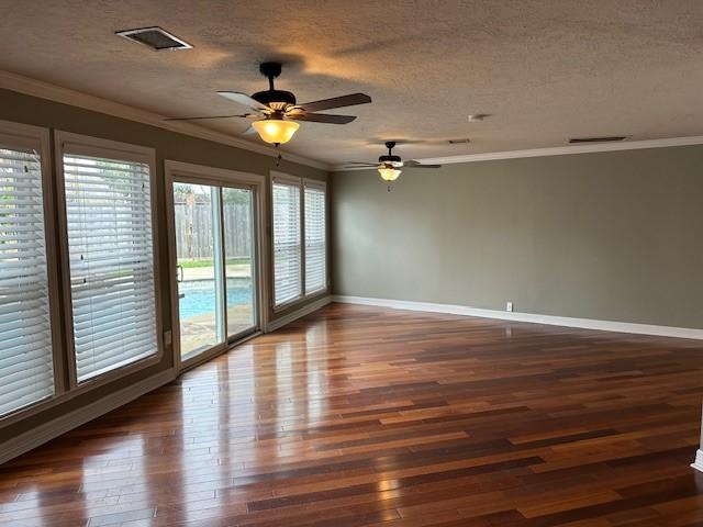 empty room featuring baseboards, visible vents, ornamental molding, wood finished floors, and a textured ceiling