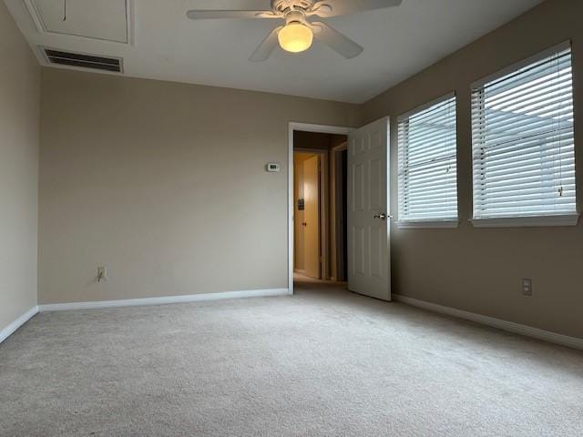 unfurnished room with light colored carpet, a ceiling fan, baseboards, visible vents, and attic access