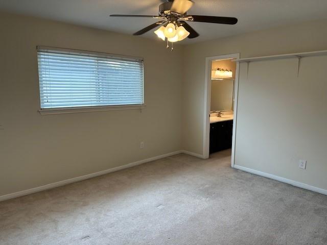 unfurnished bedroom featuring light carpet, baseboards, ceiling fan, ensuite bathroom, and a closet