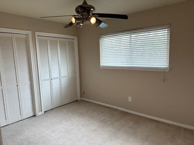 unfurnished bedroom featuring carpet flooring, ceiling fan, baseboards, and two closets