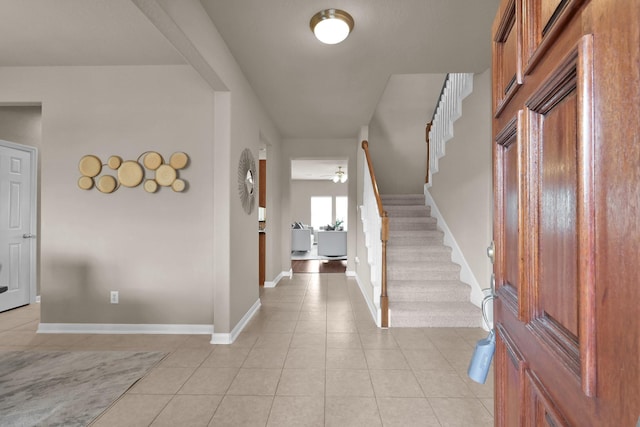 foyer entrance featuring light tile patterned floors, ceiling fan, stairs, and baseboards