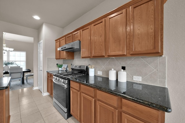 kitchen featuring under cabinet range hood, stainless steel gas range oven, tasteful backsplash, and brown cabinetry