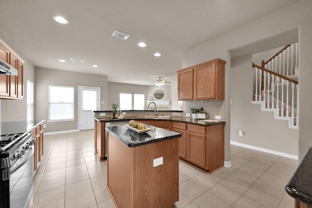 kitchen featuring stainless steel range with gas cooktop, visible vents, backsplash, a sink, and a peninsula