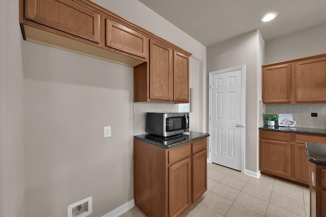 kitchen with brown cabinets, stainless steel microwave, backsplash, and dark stone countertops