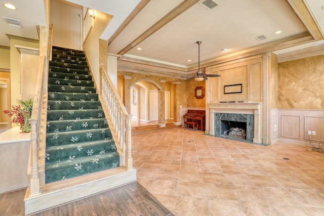 unfurnished living room featuring arched walkways, a wainscoted wall, visible vents, a decorative wall, and ornamental molding