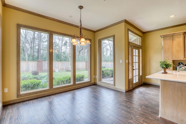 unfurnished dining area featuring a healthy amount of sunlight, dark wood-style floors, crown molding, and a notable chandelier