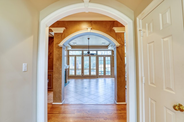 hall with crown molding, arched walkways, and wood finished floors