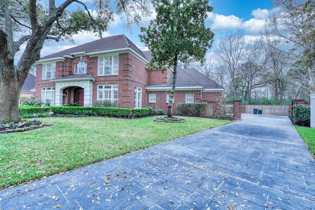 colonial house featuring brick siding, decorative driveway, a front yard, and fence