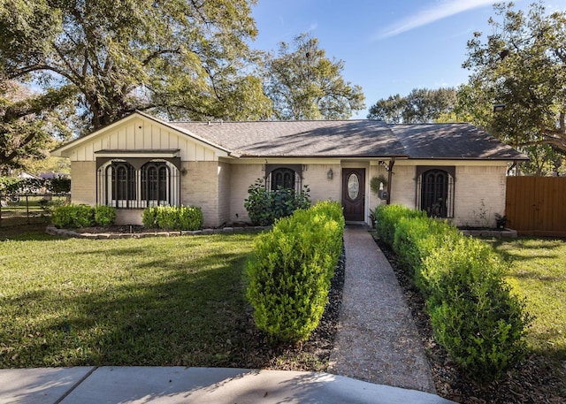 ranch-style house featuring brick siding, a shingled roof, board and batten siding, fence, and a front lawn