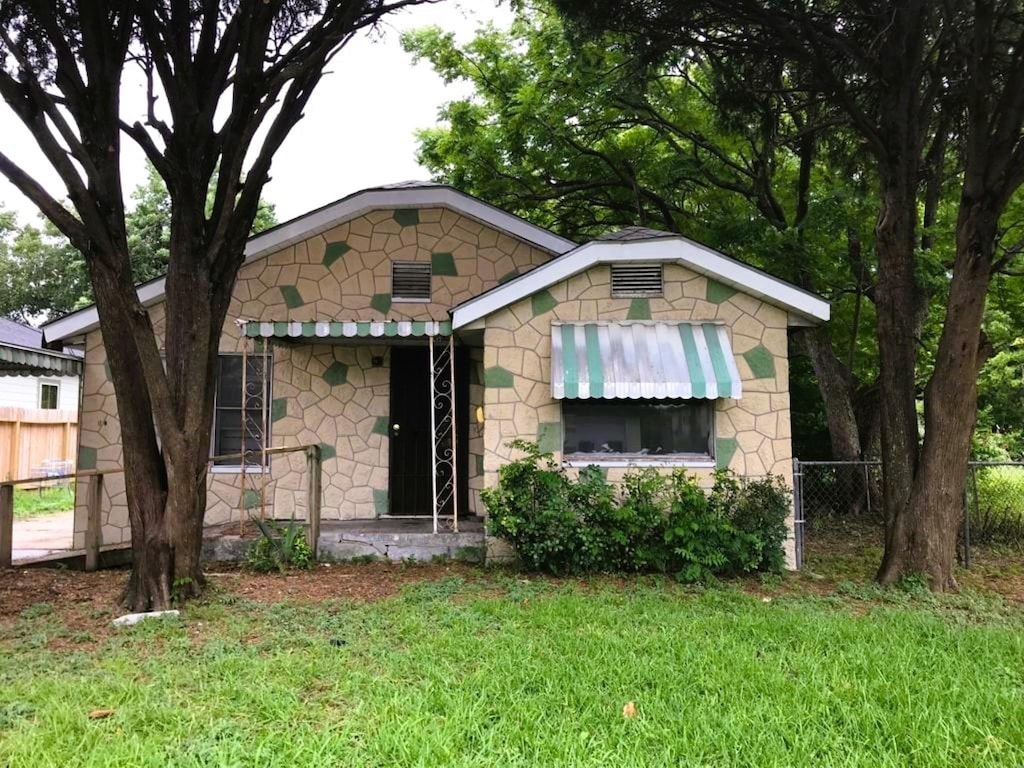 view of front facade with stone siding, fence, and a front yard