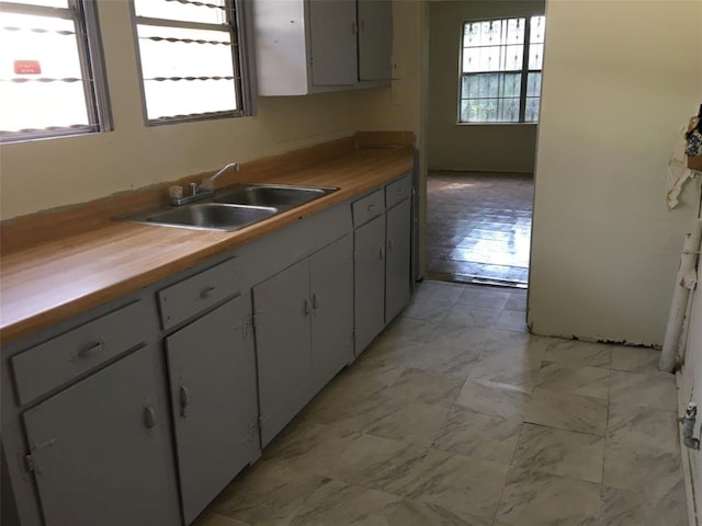 kitchen with marble finish floor, butcher block counters, white cabinetry, and a sink