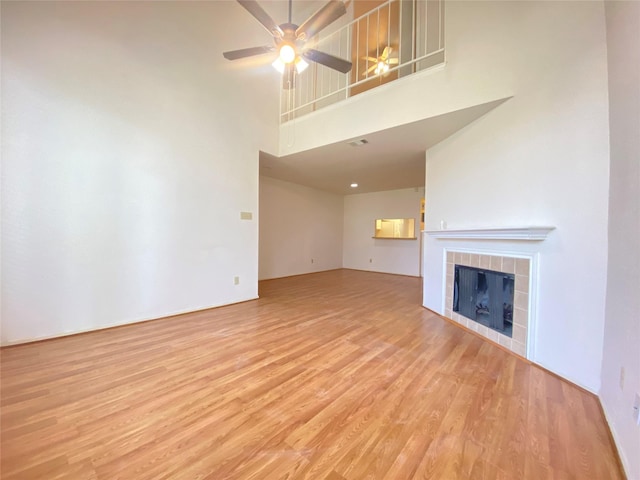 unfurnished living room with a towering ceiling, a tile fireplace, light wood-style flooring, and a ceiling fan