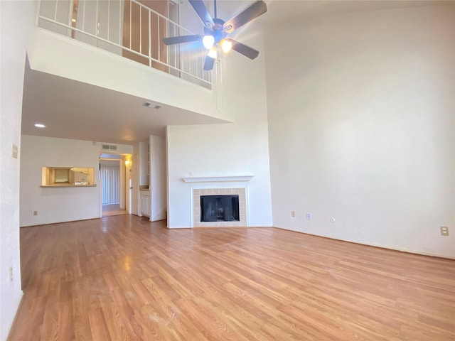 unfurnished living room with ceiling fan, a tiled fireplace, wood finished floors, and visible vents