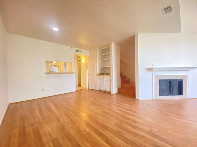 unfurnished living room featuring stairway, light wood-type flooring, a tile fireplace, and visible vents