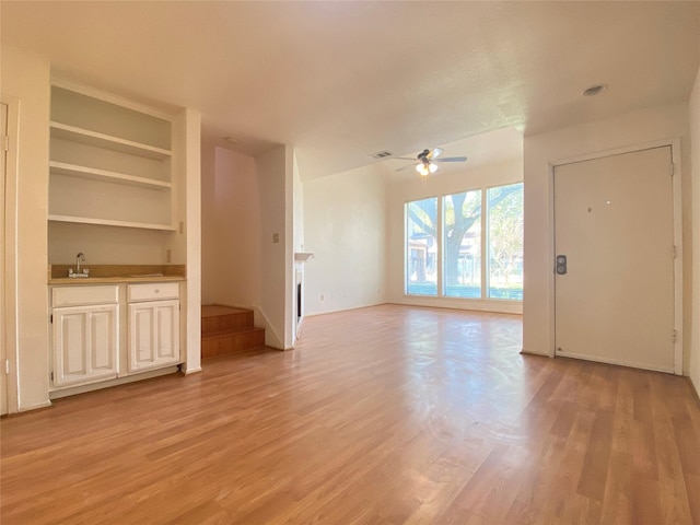 unfurnished living room with light wood-type flooring, a sink, visible vents, and a ceiling fan