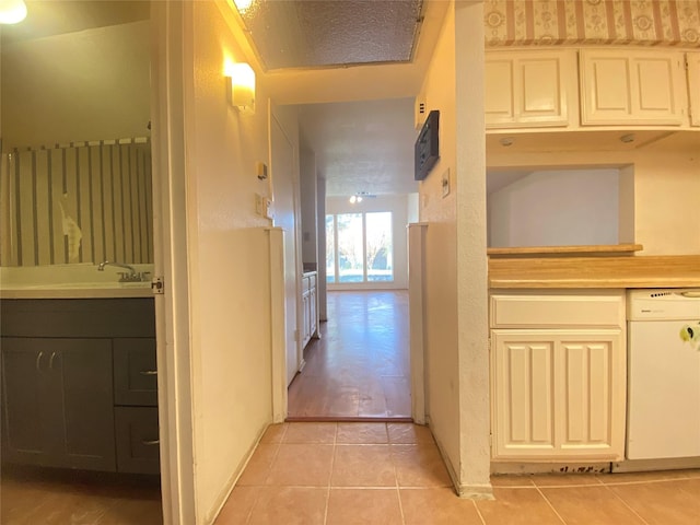 hall featuring baseboards, a sink, and light tile patterned flooring