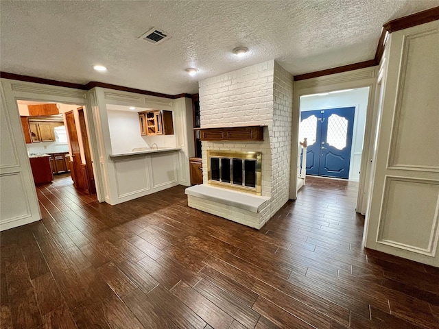 unfurnished living room featuring visible vents, dark wood finished floors, a fireplace, ornamental molding, and a decorative wall