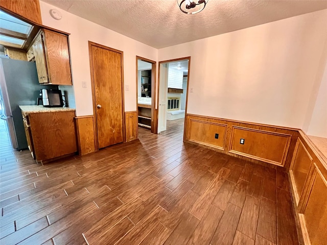 interior space with a wainscoted wall, dark wood-style flooring, and a textured ceiling