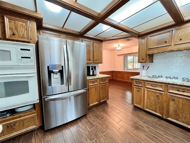 kitchen featuring a wainscoted wall, white appliances, brown cabinetry, decorative backsplash, and dark wood-style flooring