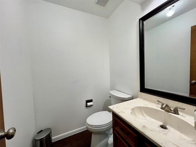 half bathroom with visible vents, toilet, wood finished floors, baseboards, and vanity