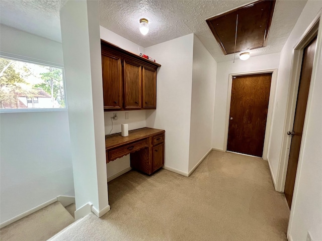 interior space with baseboards, light carpet, a textured ceiling, and attic access