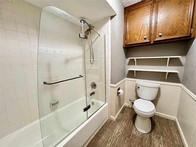 full bath with toilet, wood finished floors, shower / bathtub combination, and wainscoting