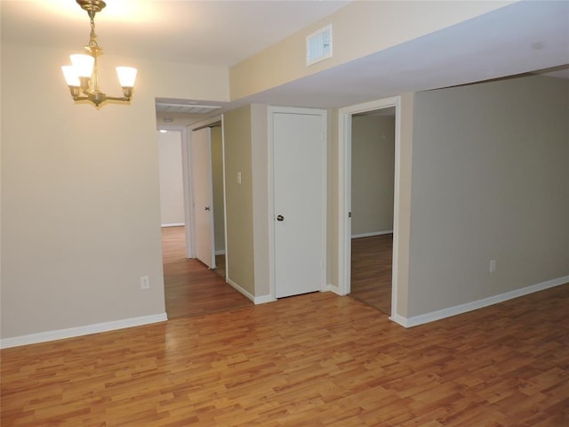 unfurnished room with a notable chandelier, light wood finished floors, visible vents, and baseboards