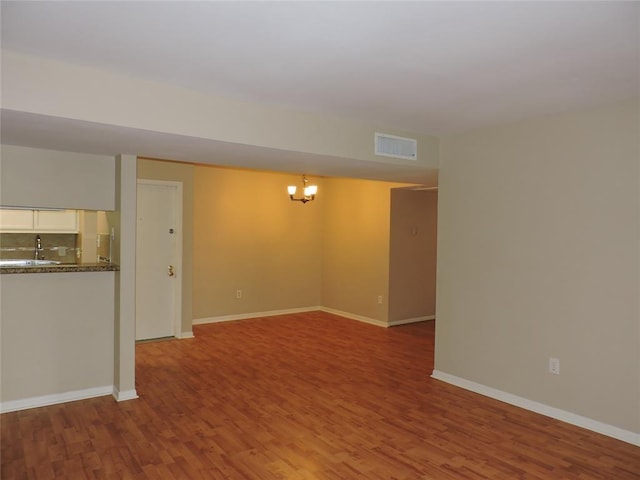 empty room featuring an inviting chandelier, visible vents, baseboards, and wood finished floors